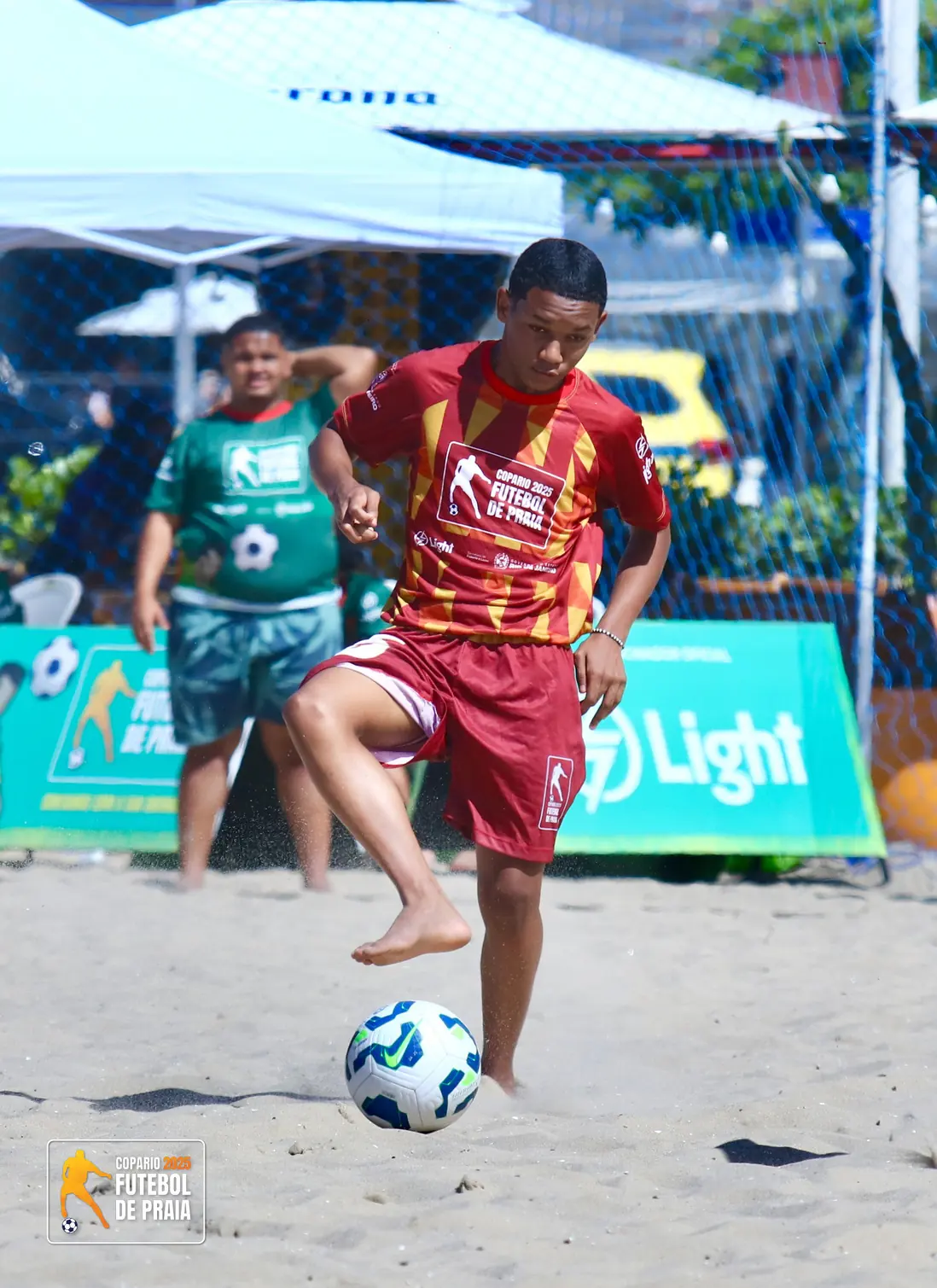 Jogador de camisa vermelha faz embaixadinha na areia