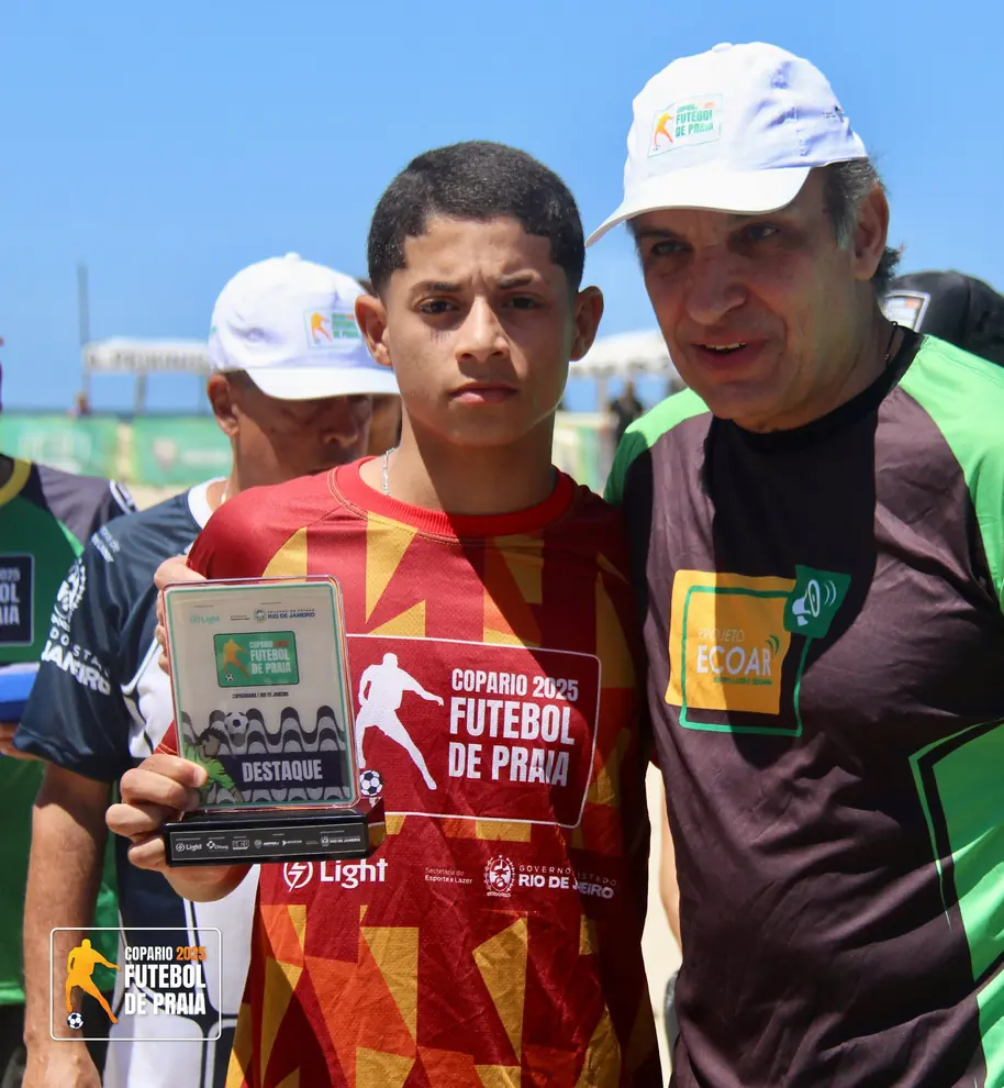 Garoto de camisa vermelha segura troféu ao lado de um treinador
