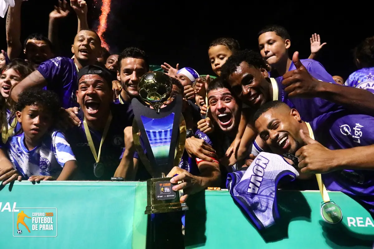 Jogadores de camisa roxa e azul comemoram o título com o troféu ao entardecer