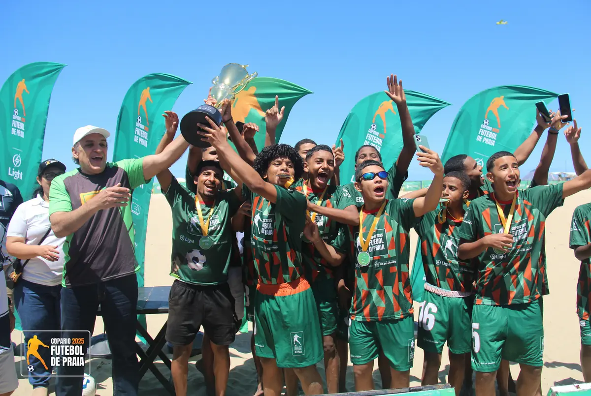 Equipe de camisa verde e laranja ergue o troféu de campeã na areia