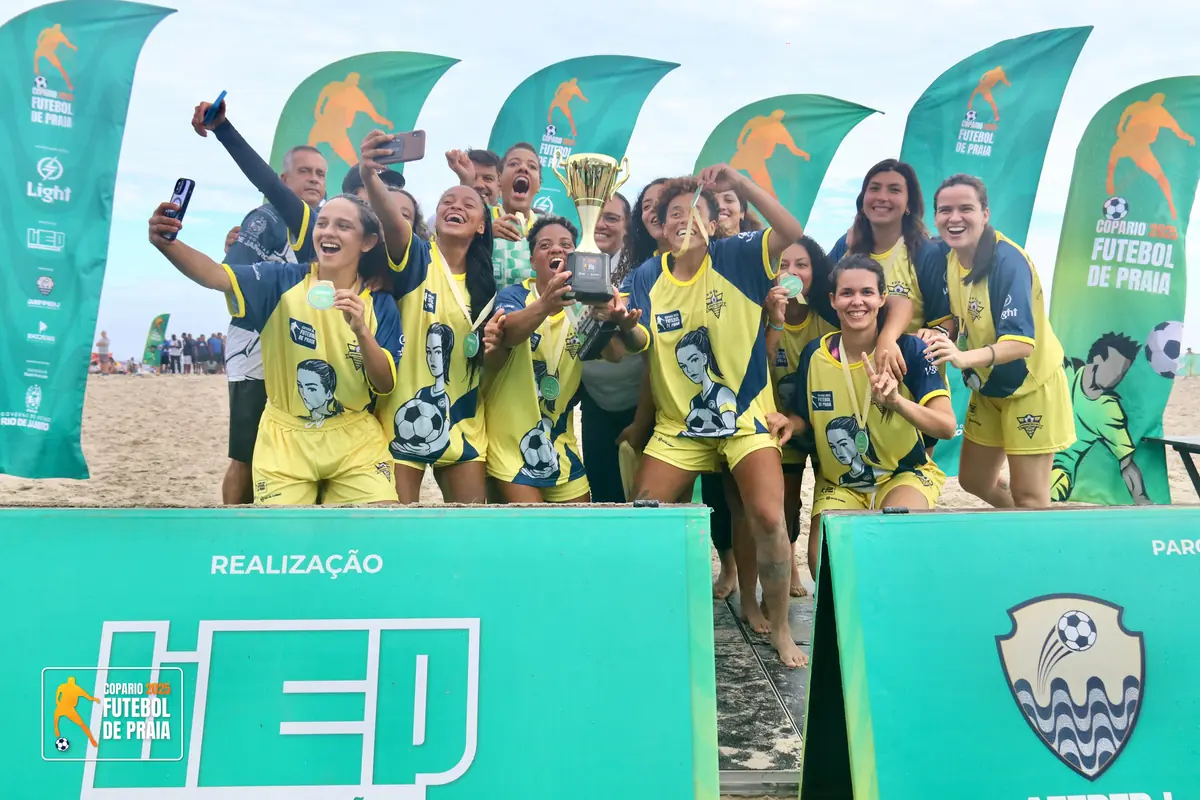Equipe de camisa amarela posa com medalhas em frente ao painel dos patrocinadores