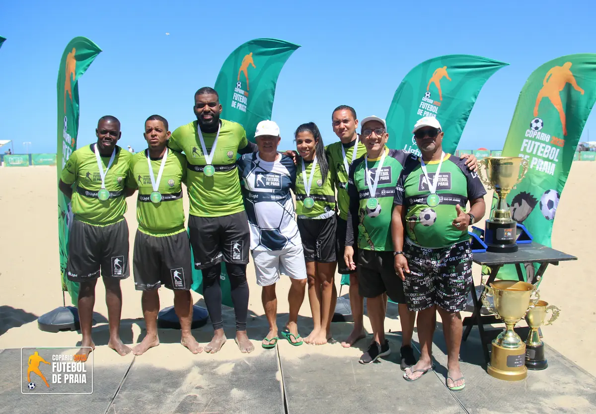 Equipe técnica posa com medalhas e troféus sob as bandeiras do torneio