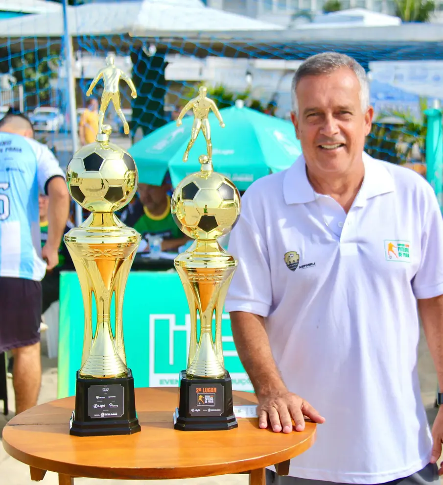 Homem de camisa branca ao lado de dois troféus dourados