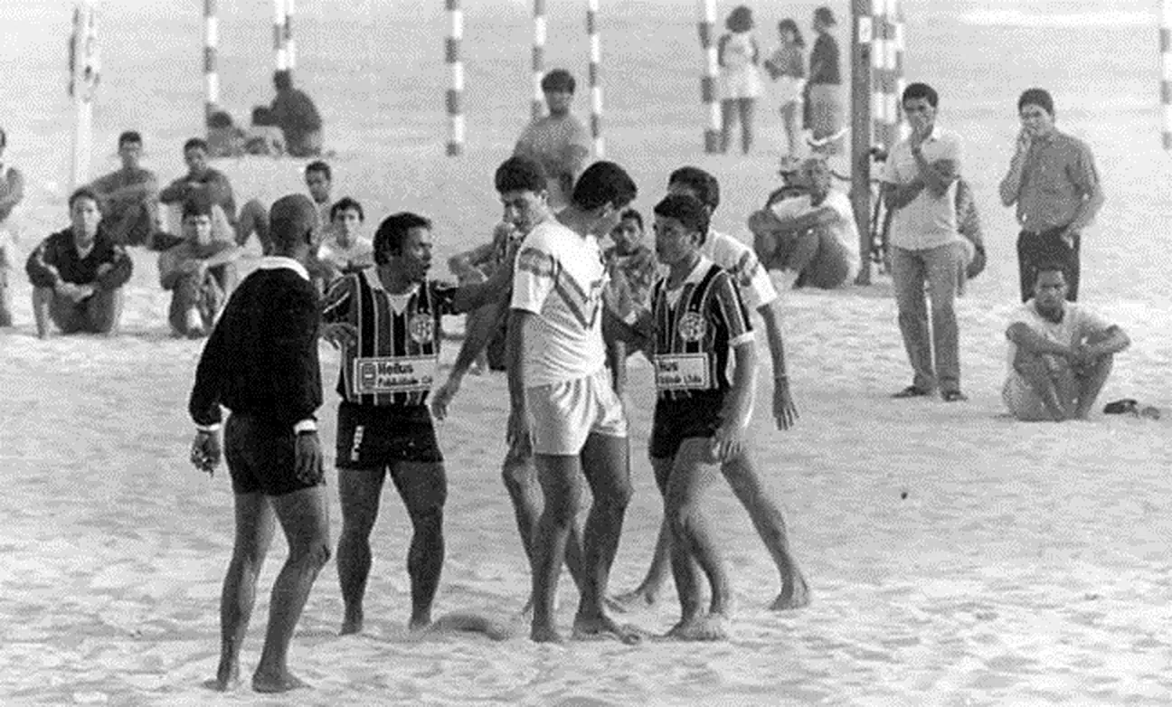 Foto em preto e branco de jogadores uniformizados e árbitro em partida em 1990